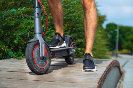 Close Up Of Man Riding Electric Kick Scooter At Beautiful Park Landscape. Man Is On Foreground, Modern Park is on Background And Blurred.の写真素材