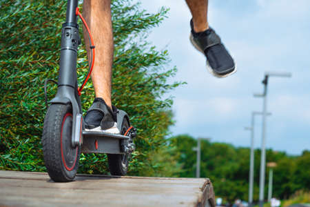 Close Up Of Man Legs Riding Electric Kick Scooter At Beautiful City Park Outdoors And Rising Footの写真素材