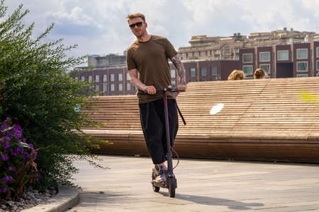 Atractive Man On Vacation Having Fun Driving Electric Scooter Outdoors In Modern Park.の写真素材