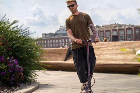 Handsome Young Man On Vacation Having Fun Driving Electric Scooter Outdoors In Modern Park.の写真素材