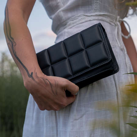 Woman holding qulted black clutch at natural green background.の写真素材