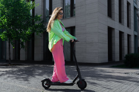 Young attractive blond woman riding electrick kick scooter at modern cityscapeの写真素材