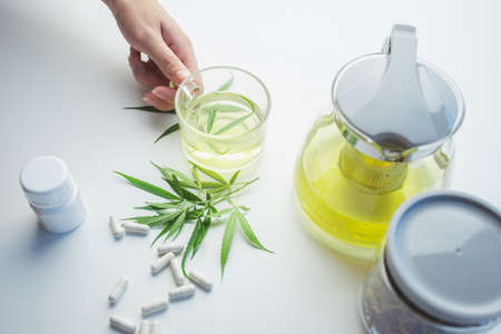 Hand pick cup hot drink made by infusing the fresh leaves of the marijuana leaf in boiling water. Beverage ganja in cup for drink. Marijuana and capsules drug. Concept alternative herbs for healing.の写真素材