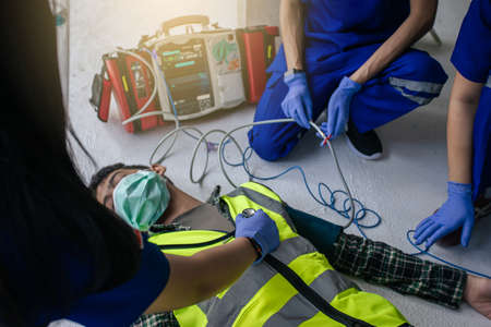 Team work medical emergency use Automated External Defibrillator (AED) being operated on during help unconscious worker accident in construction site.の写真素材