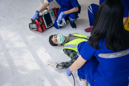 Team work medical emergency use Automated External Defibrillator (AED) being operated on during help unconscious worker accident in construction site.の写真素材