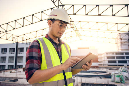 Asian man engineer contractor in construction site work during inspection for estimate price for renovated structure. Engineer use tablet for working in construction site work.の写真素材