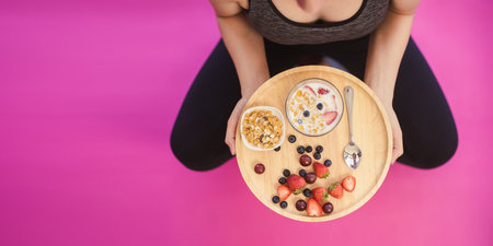 Fitness sport woman in fashion sportswear eating healthy breakfast bowl. Fresh and dry fruits and honey in clear ceramic bowl in fitness sport woman hands. Clean eating, dieting and healthy concept.の写真素材