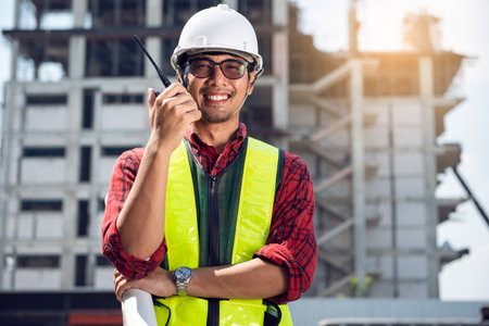 Asian young engineer glasses smiling wear a safety helmet equipment and drawing on hand with radio communication.の写真素材