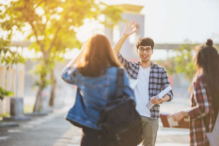 Group Asian young student, Asian man holding book and greeting with friend outdoor under sunlight.の写真素材