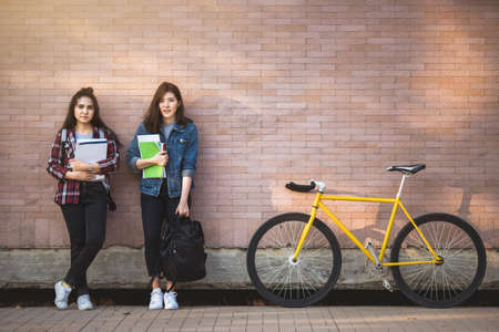 Two Asian young student holding book standing outdoor near wall background.