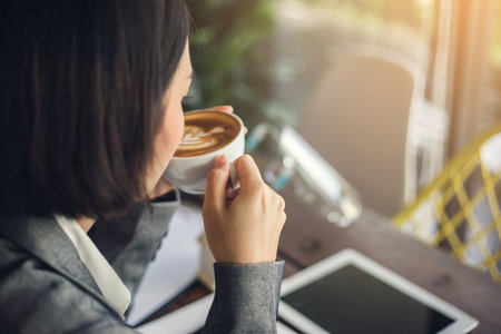 Back view businesswoman drinking a latte at table in coffee shop.の写真素材