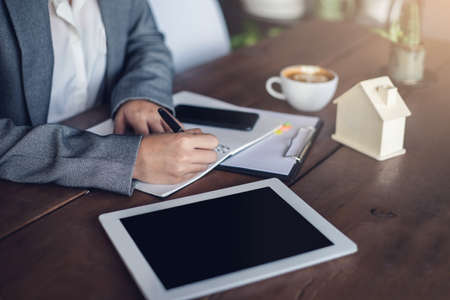 Closeup hand of businesswoman writing on paper real estate documents with tablet and smartphone. New normal work from home.の写真素材