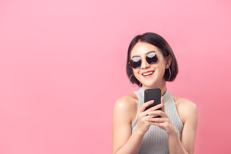 Asian woman short hair her smile and holding  smartphone in studio pink background.の写真素材