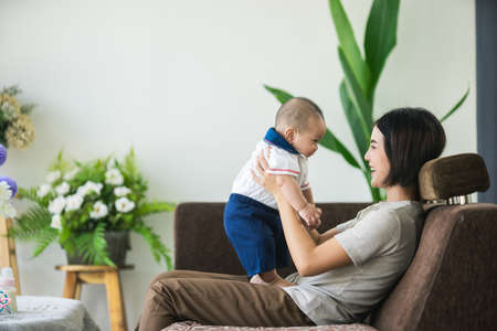 Asian mother lifting and playing with newborn baby, Happy mom and baby plying in living room.の写真素材