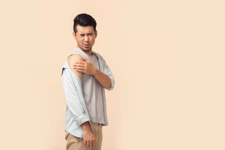 Portrait Asian man feeling injury shows a bandage after getting a vaccination during immunization program on brown background.の写真素材
