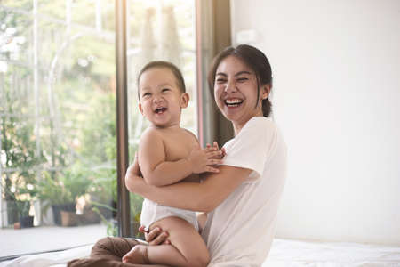 Asian mom and baby smiling happiness in living room together. Female stay at home with her son. Mom and baby in motherâs day concept.の写真素材