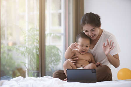 Asian mother and her son smiling together using tablet for online media. Asian mom and baby  show...