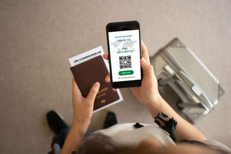 Selective focus, Smartphone on hand of traveler show health passport of vaccination certification in the airport. Online certificate of vaccinated coronavirus. Travel concept during Covid-19 pandemic.の写真素材