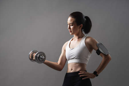 Portrait athlete Asian active woman workout with dumbbell weightlifting in studio grey background....