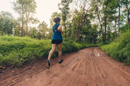 Trail running athlete through the in the rural road and tropical. Active woman trail runner running in the forest in the morning.の写真素材