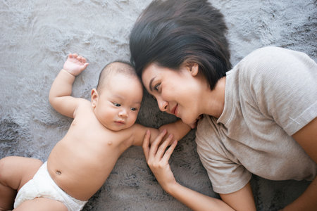 Happy Asian mom playing with newborn lying together stay at home in Motherâs Day concept.の写真素材