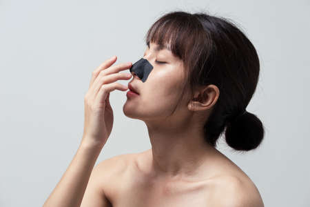 Asian woman applying mask charcoal deep cleansing nose pore strip on fresh clean skin. Beauty and skin care treatment concept.の写真素材