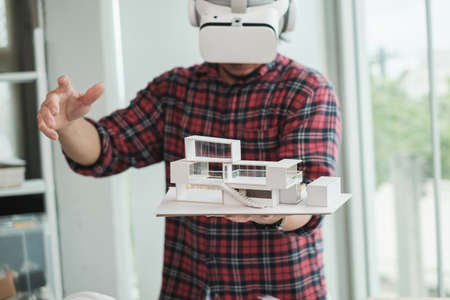 Selective focus. Architect or Engineer wearing VR headset and holding house model for working...