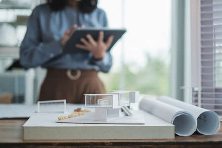 Modern house model with female Architect working use tablet for design or investment project in background at office.の写真素材