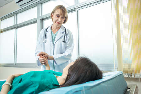 Senior doctor female standing beside the bed and talking with female patient in ward at hospital.の写真素材