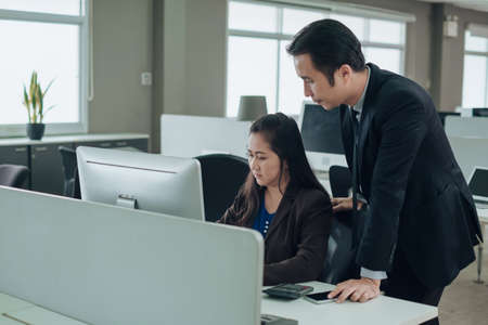 Asian woman worker with coworker working together in company office. Leadership follow up job with...