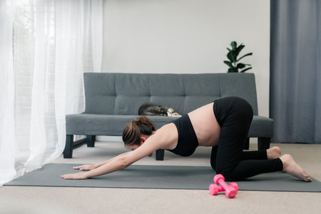 Pregnant asian woman is doing a yoga practice in downward pose. Stretching her body to keep her...