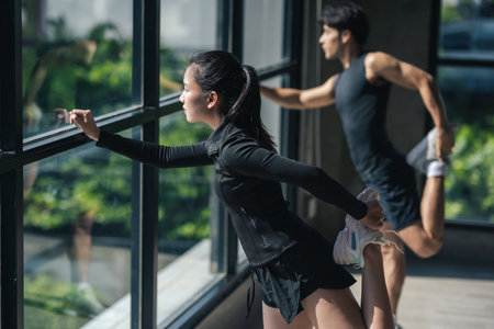Asian woman stretching before workout training with personal trainer at gym. Two Asian people...