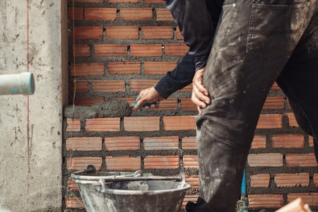 Bricklayer with trowel to installing red bricks masonry and  PVC pipe in a new wall. Blue plumbing in the cement wall of the bathroom under construction. Selective focus.の写真素材