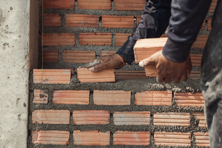 Bricklayer masonry installing red bricks in a new wall under construction.の写真素材