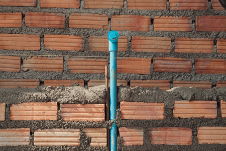 Bricklayer installing red bricks masonry and  PVC pipe in a new wall. Blue plumbing in the cement wall of the bathroom under construction.の写真素材