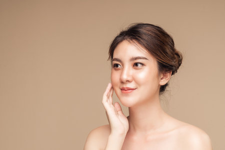 Closeup photo of a smiling brunette asian woman touching her face with natural makeup, hydrated skin, Facial face and wrinkles treatment concept.の写真素材