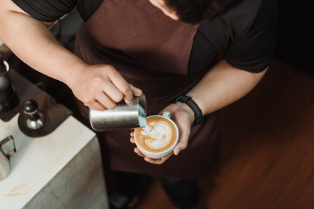 Top view, Barista pouring milk foam to making latte art coffee. Young man barista working at coffee shop. Latte art menu coffee, Espresso, Coffee menu making concept. Selective focus.の写真素材