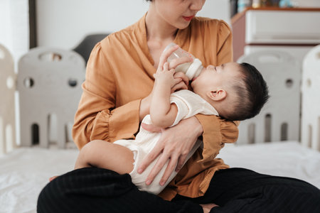 Adorable little Asian baby sleep during drinking milk from baby bottle. Asian mother holding...