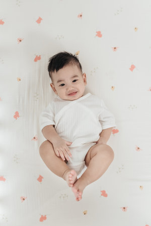 Adorable asian baby comfortable and good mood, Lying on a bed looking at camera. Baby healthcare hygiene concept.の写真素材