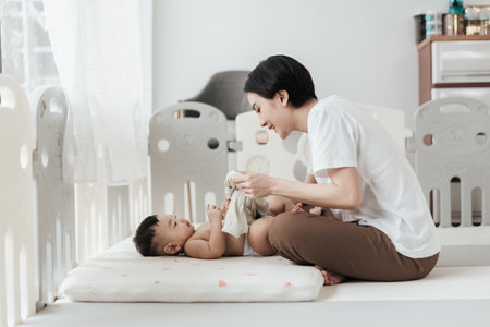Cute Asian baby wearing clothes by his mother after changing him diaper. Asian family motherâs day concept.の写真素材