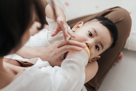 Top view, Adorable little Asian baby drinking from baby bottle. Mother holding adorable her son with milk feeding from milk bottle. Concept babies healthcare.の写真素材