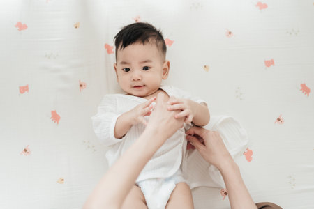 Top view mother wearing clothes to her baby. Asian family motherâs day. Baby healthcare hygiene concept.の写真素材
