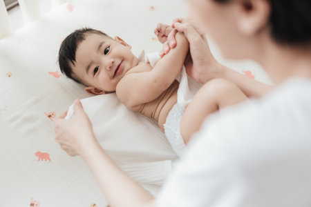 Top view mother wearing clothes to her baby. Asian family motherâs day. Baby healthcare hygiene concept.の写真素材