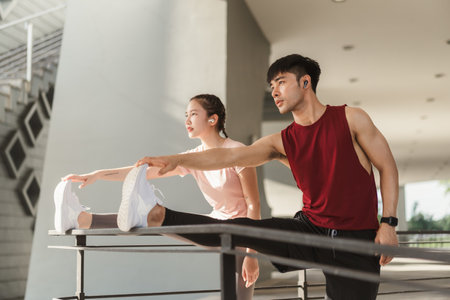 Two Asian young athlete man and woman in sportswear doing stretching together before jogging exercise in urban area. Warming up for workout outdoor in the morning.の写真素材