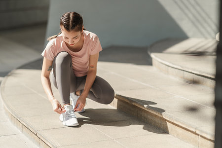 Young Asian woman tying shoelace on her running shoes. Preparation before jogging exercise. Fitness and sport activity. Healthy exercise concept.の写真素材