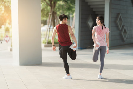 Young Asian couple in sportswear doing stretching together before jogging exercise in urban area. Warming up for workout outdoor in the morning.の写真素材
