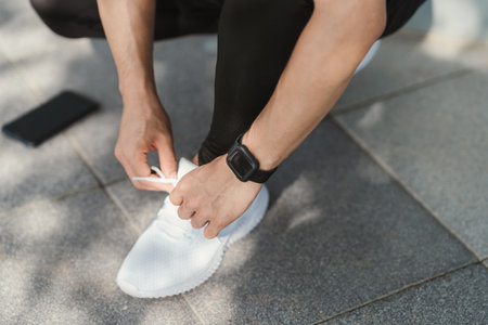 Preparation before jogging. Closeup hand of athletic male tying shoelace on running shoes. Fitness and sport activity. Healthy exercise concept.の写真素材