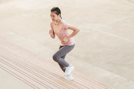 Full length sporty young Asian woman running on steps. Young female in sportswear jogging while exercising on the steps outdoor.の写真素材