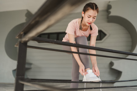 Young Asian woman tying shoelace on her running shoes. Preparation before jogging exercise. Fitness...