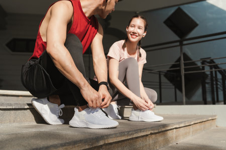 Preparation before jogging exercise. Together young Asian man and woman tying shoelace on her running shoes. Fitness and sport activity. Healthy exercise concept.の写真素材